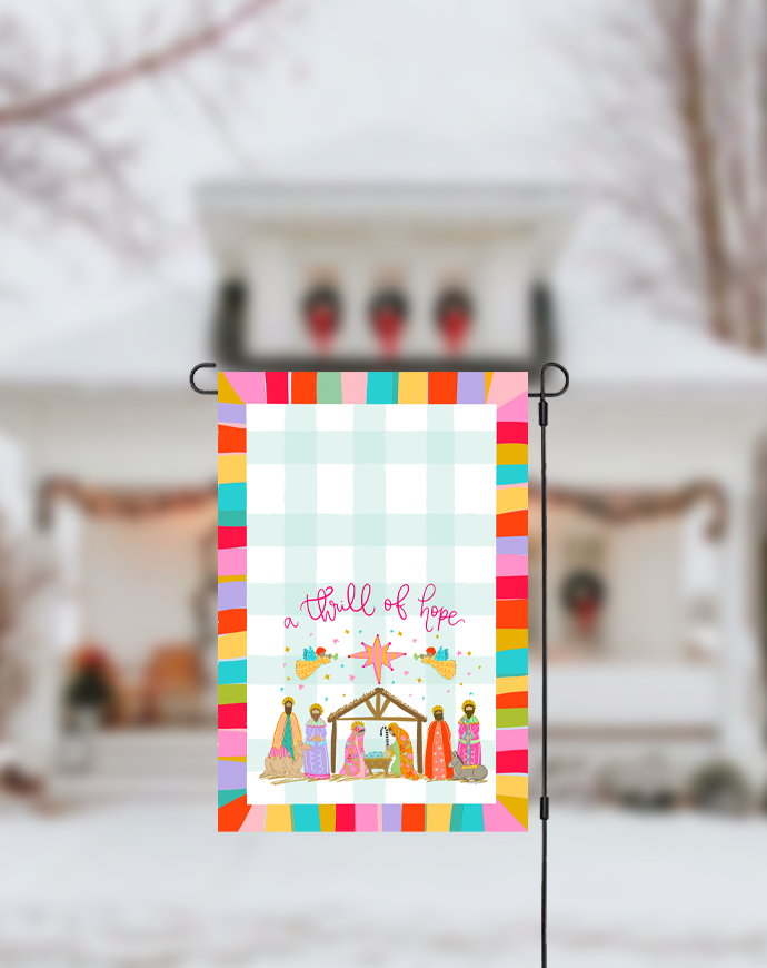 Decorative garden flag with nativity scene design in front of a snowy house.