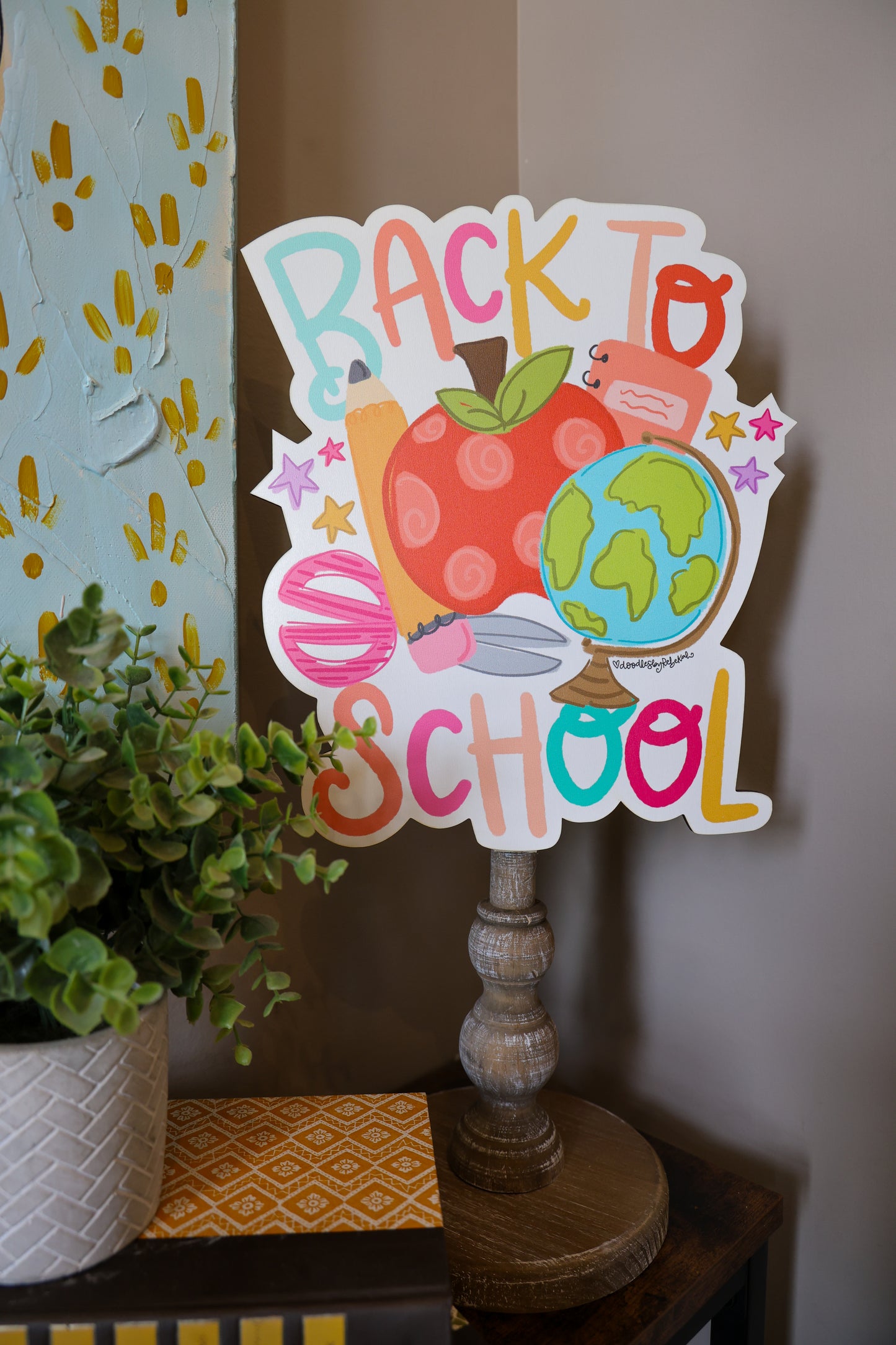 Decorative sign with 'Back to School' text on a wooden stand with a plant in the background.
