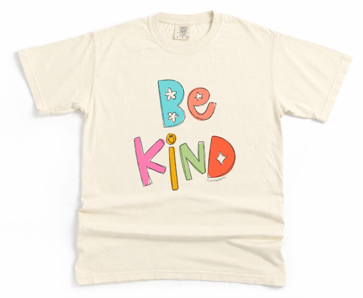 Beige t-shirt with 'Be Kind' text in colorful letters on a white background