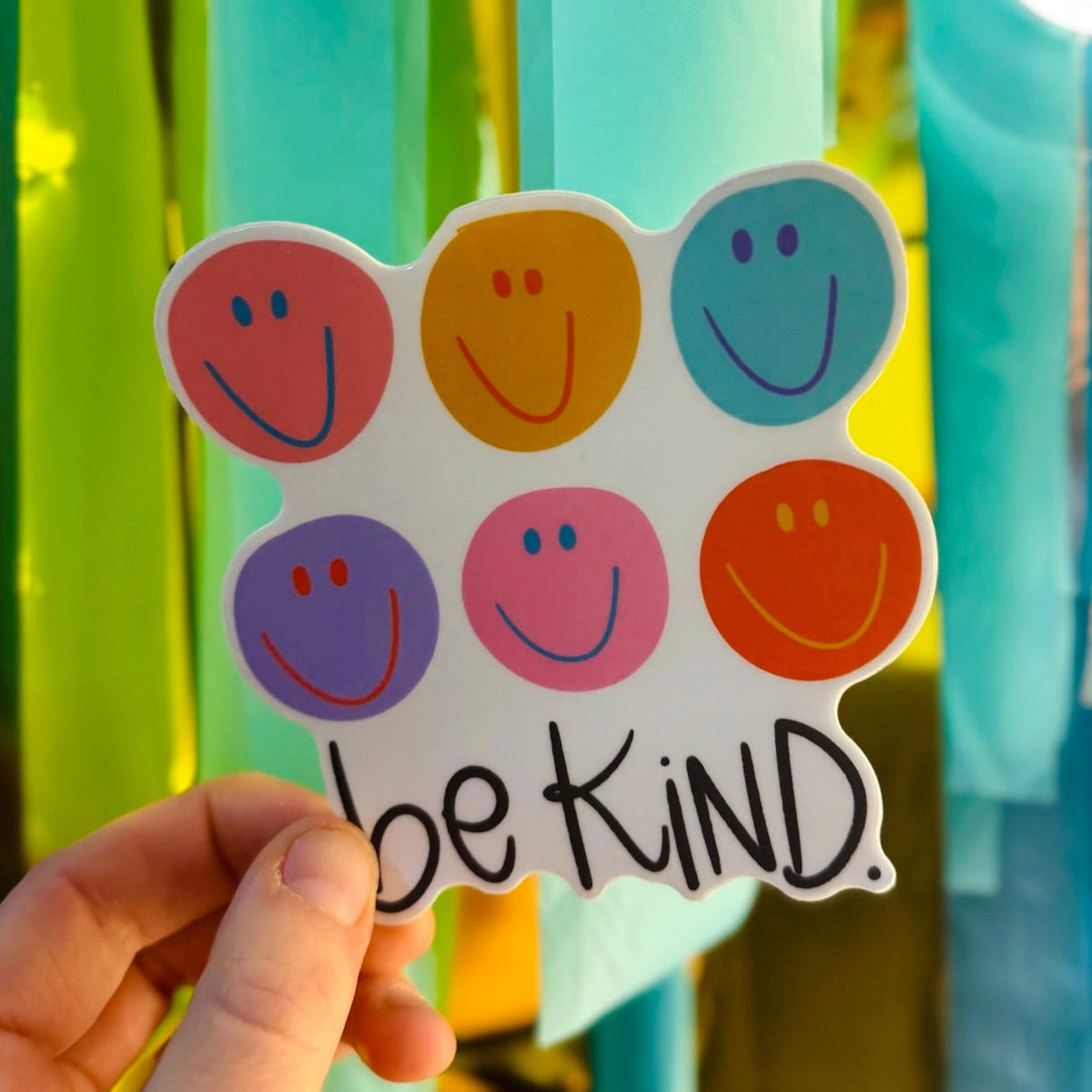Doodles by Rebekah "be KiND" colorful smiley face sticker. This hand-painted vinyl decal features six multi-colored smileys and a motivational kindness quote, making it a perfect positive gift for water bottles, laptops, and student planners.