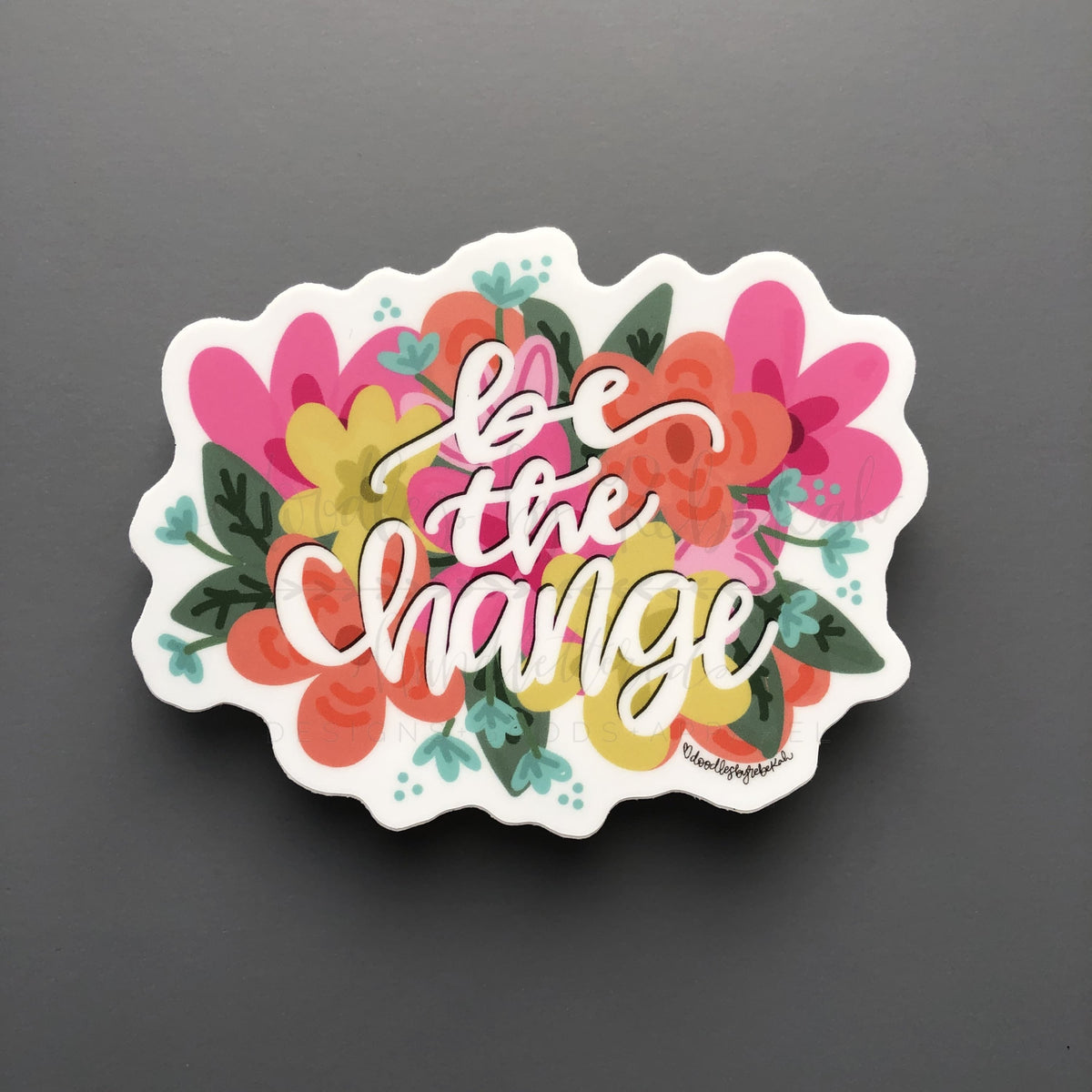A sticker with a floral border and the text 'Be The Change' in the center.
