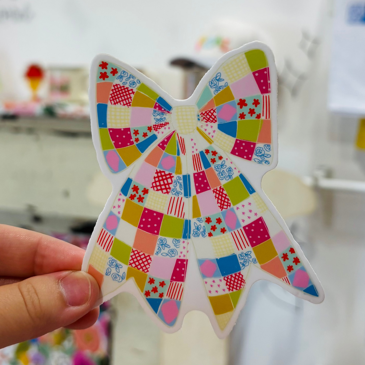 a hand holding a brightly colored plaid bow sticker