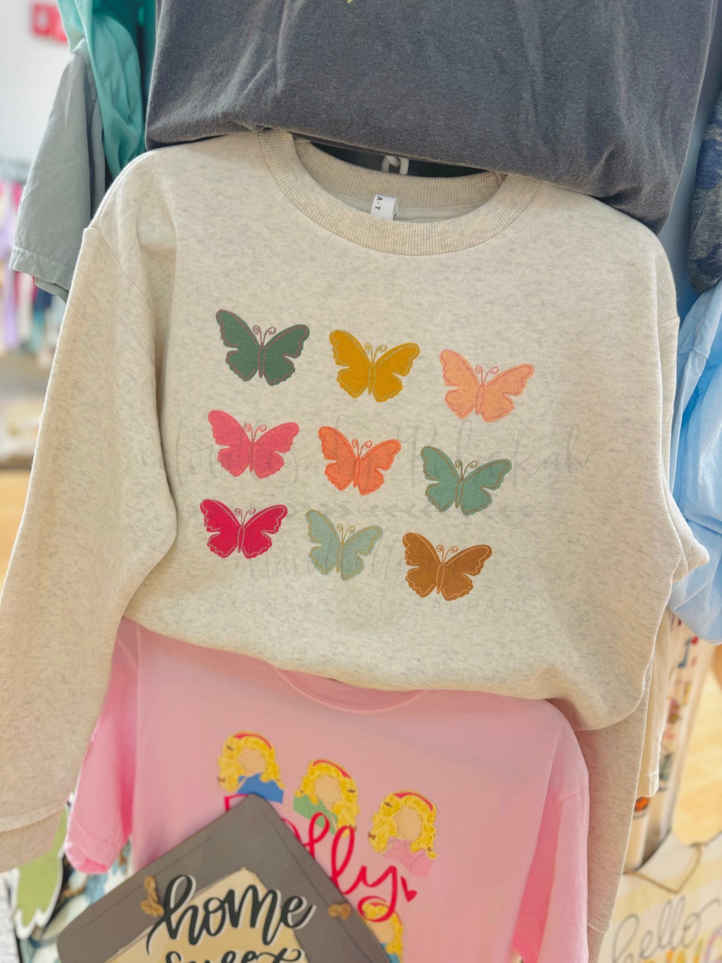 A beige sweatshirt with a pattern of multicolored butterflies on the front displayed on a mannequin.