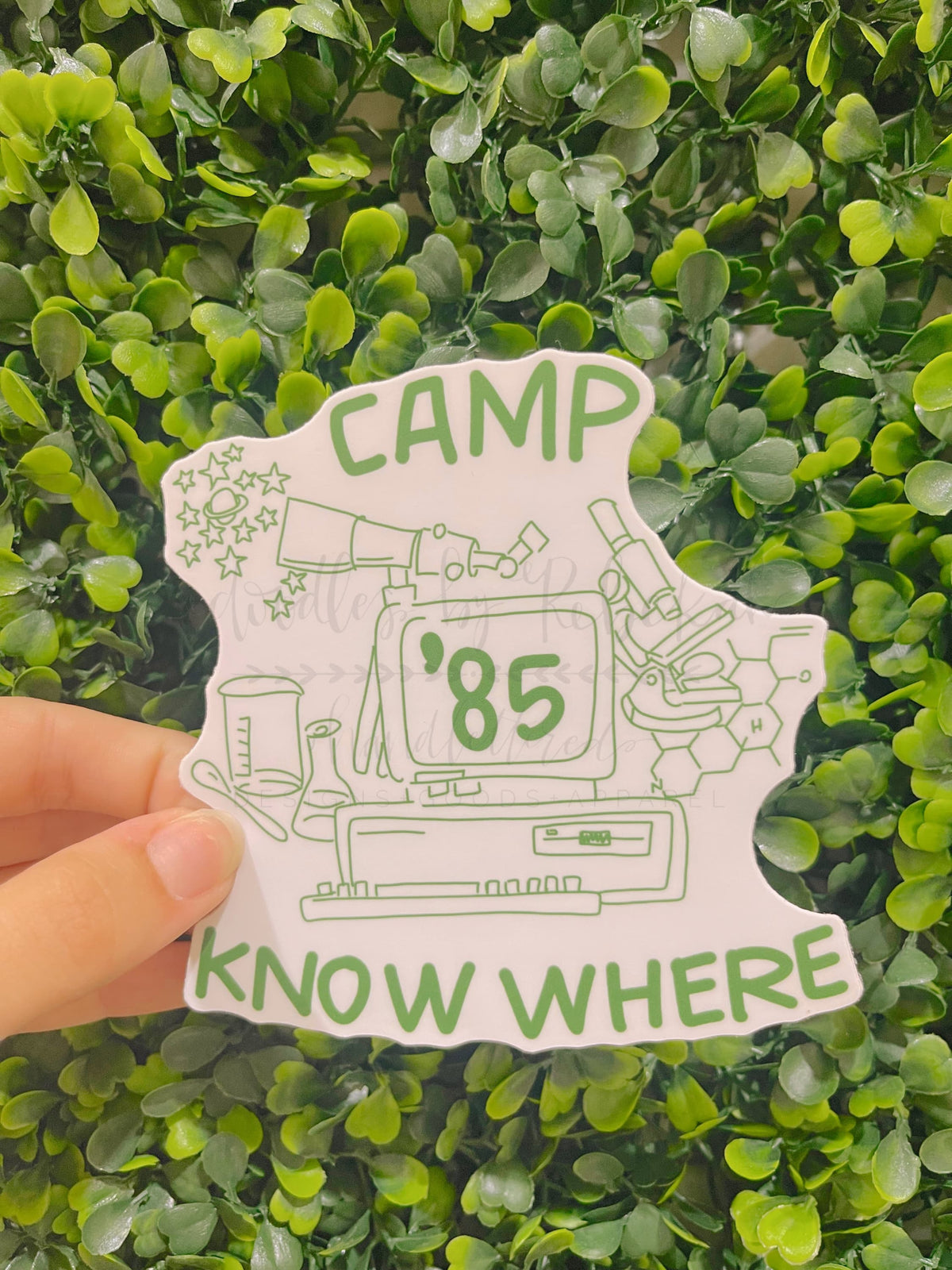 A white die cut sticker that reads "Camp Know Where '85" with a science based sketch