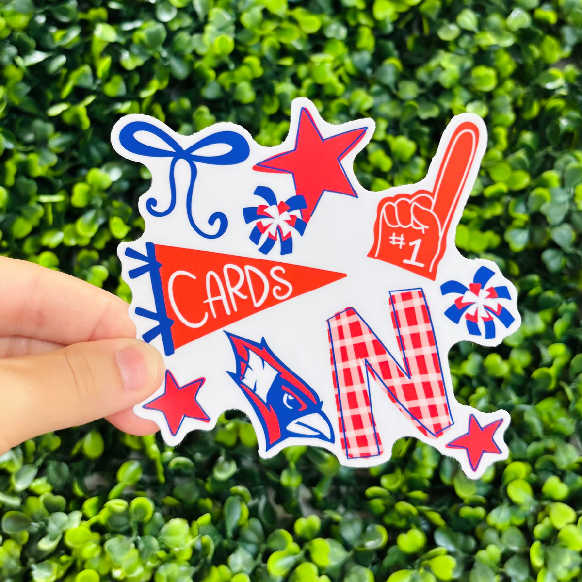A hand holding a red and blue Cardinals sticker with game day iconography