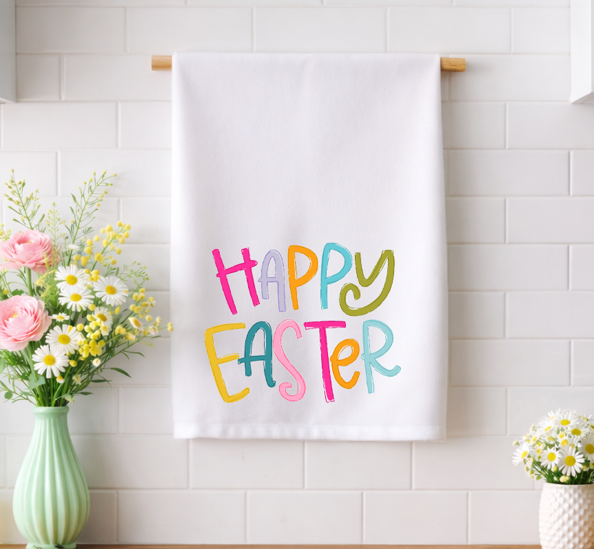 Whimsical "Happy Easter" decorative tea towel with colorful hand-drawn typography, hanging in a bright spring kitchen with fresh floral accents.
