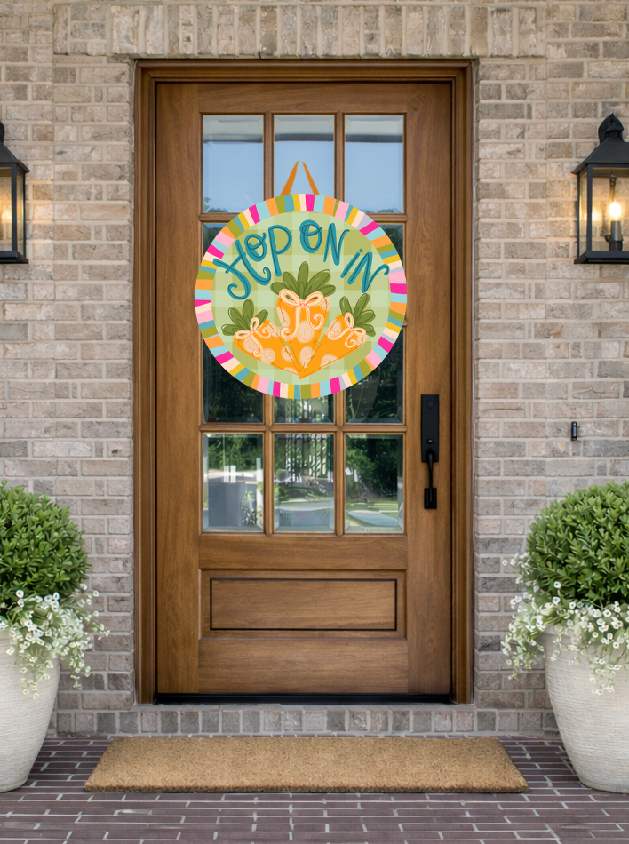 Doodles by Rebekah "Hop On In" Easter door decor featuring whimsical carrots and a green gingham pattern on a rustic front porch.