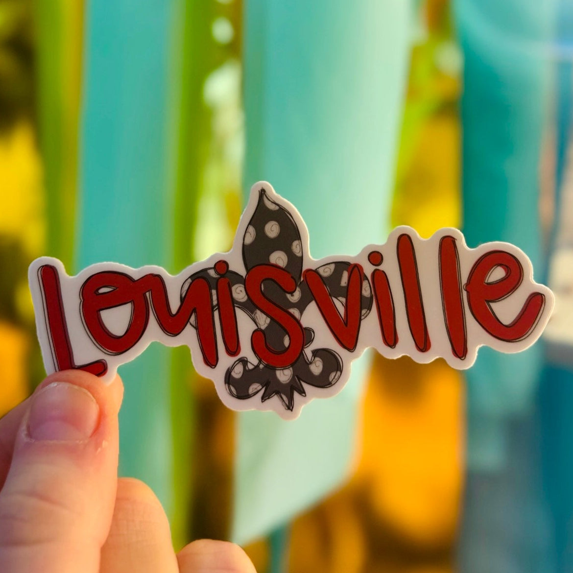 Doodles by Rebekah Louisville, Kentucky city pride sticker. This whimsical hand-painted vinyl decal featuring a polka-dot fleur-de-lis and red typography is a perfect gift for Louisville residents to decorate water bottles, laptops, and planners.