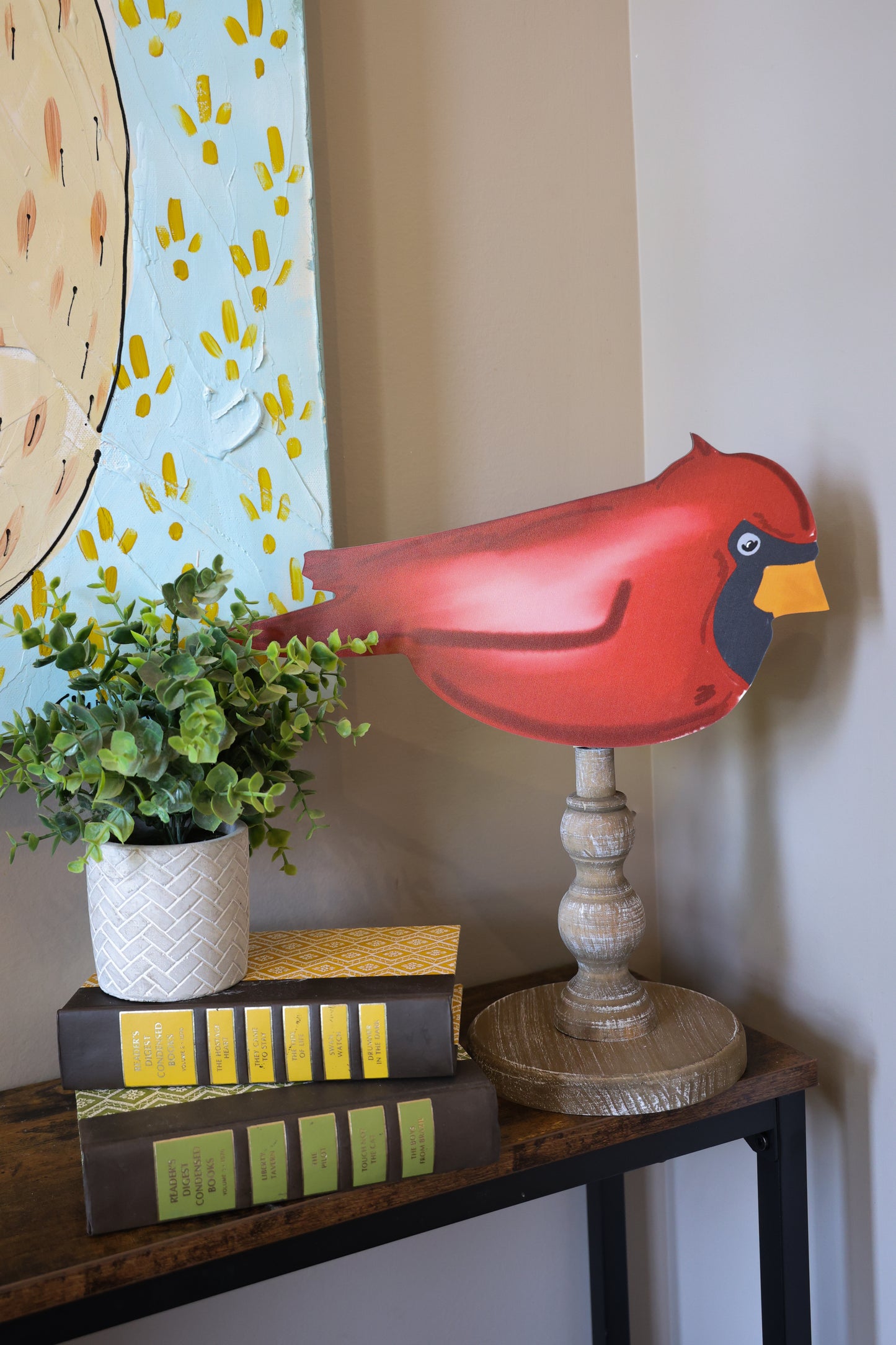 Decorative red cardinal bird on a stand with books and a plant on a table.