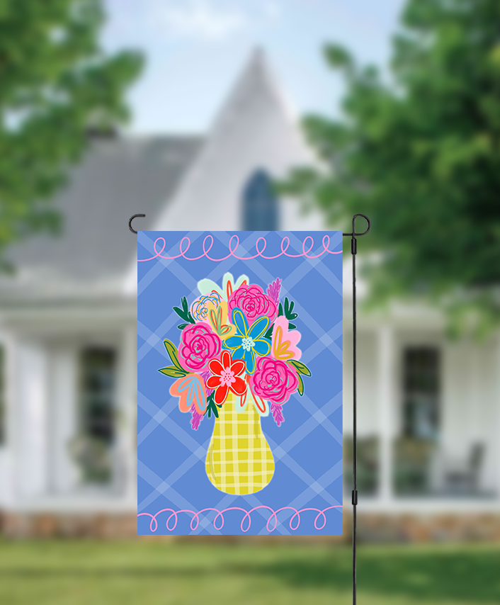 Decorative garden flag with colorful floral design on a blue background, displayed outdoors.