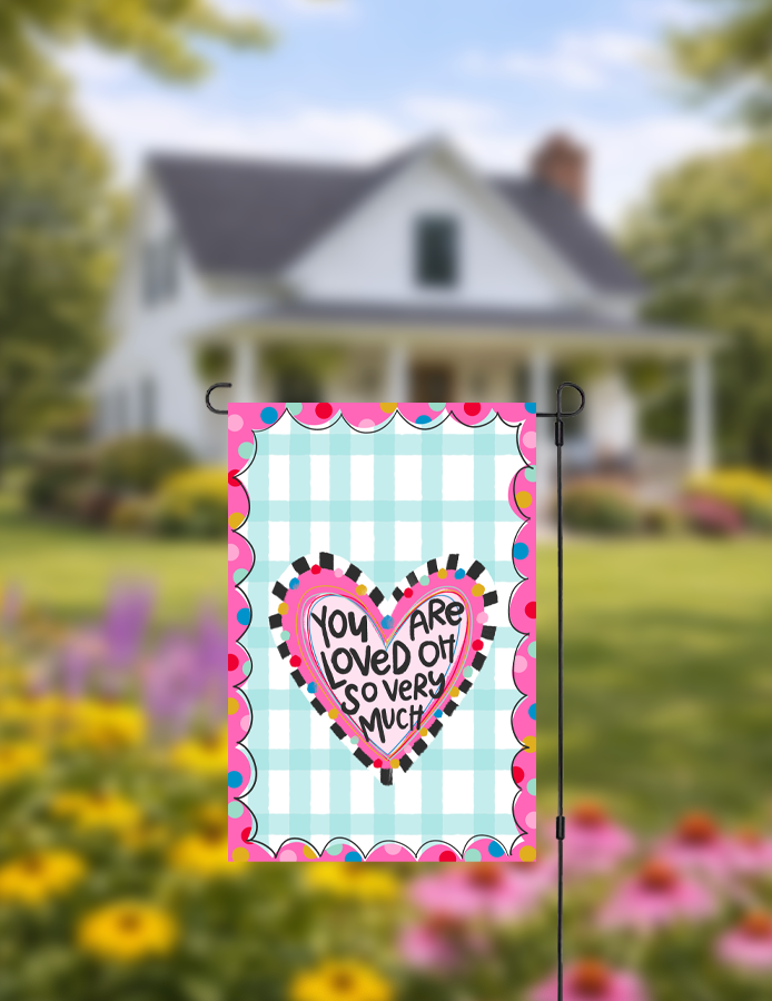 Decorative garden flag with a heart design and text in a garden setting.