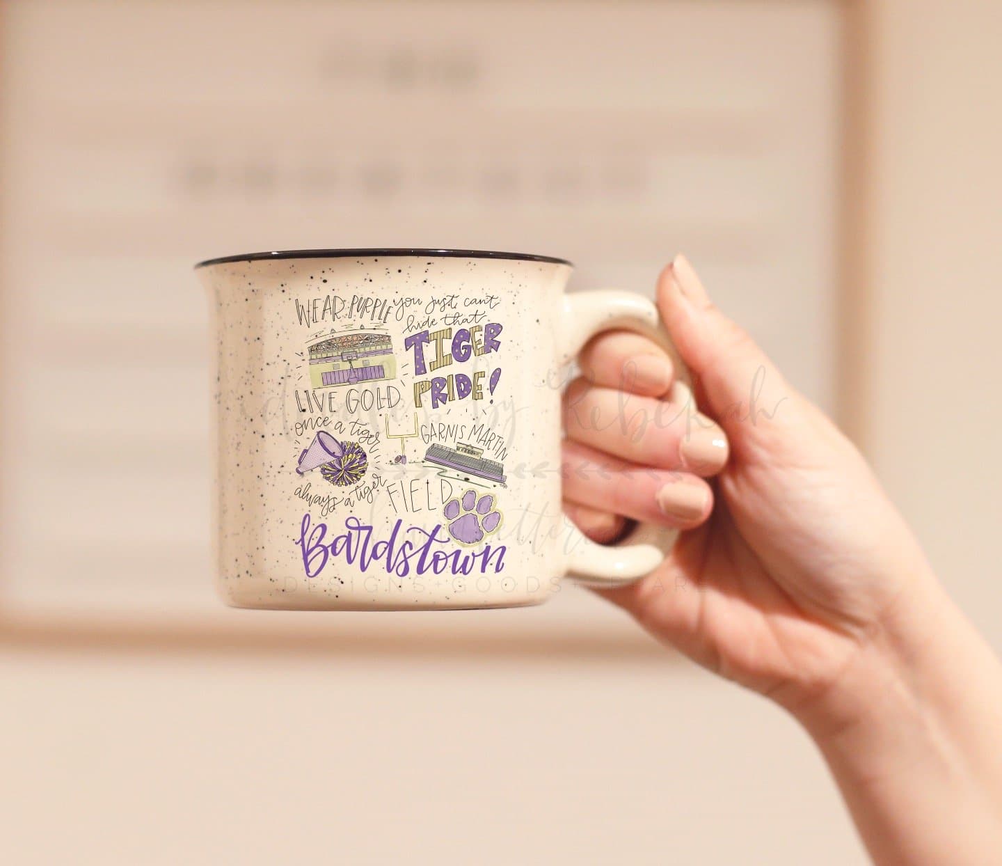 A hand holding a white ceramic coffee mug with purple and black text, featuring an illustration of a tiger and the text 'BARDSTOWN HIGH SCHOOL PRIDE'.