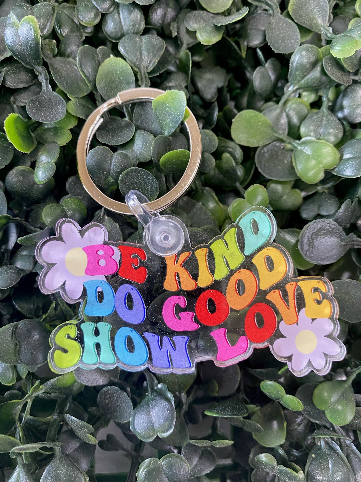 A multicolored acrylic keychain with the text 'BE KIND DO GOOD SHOW LOVE' printed on it, attached to a metal ring.