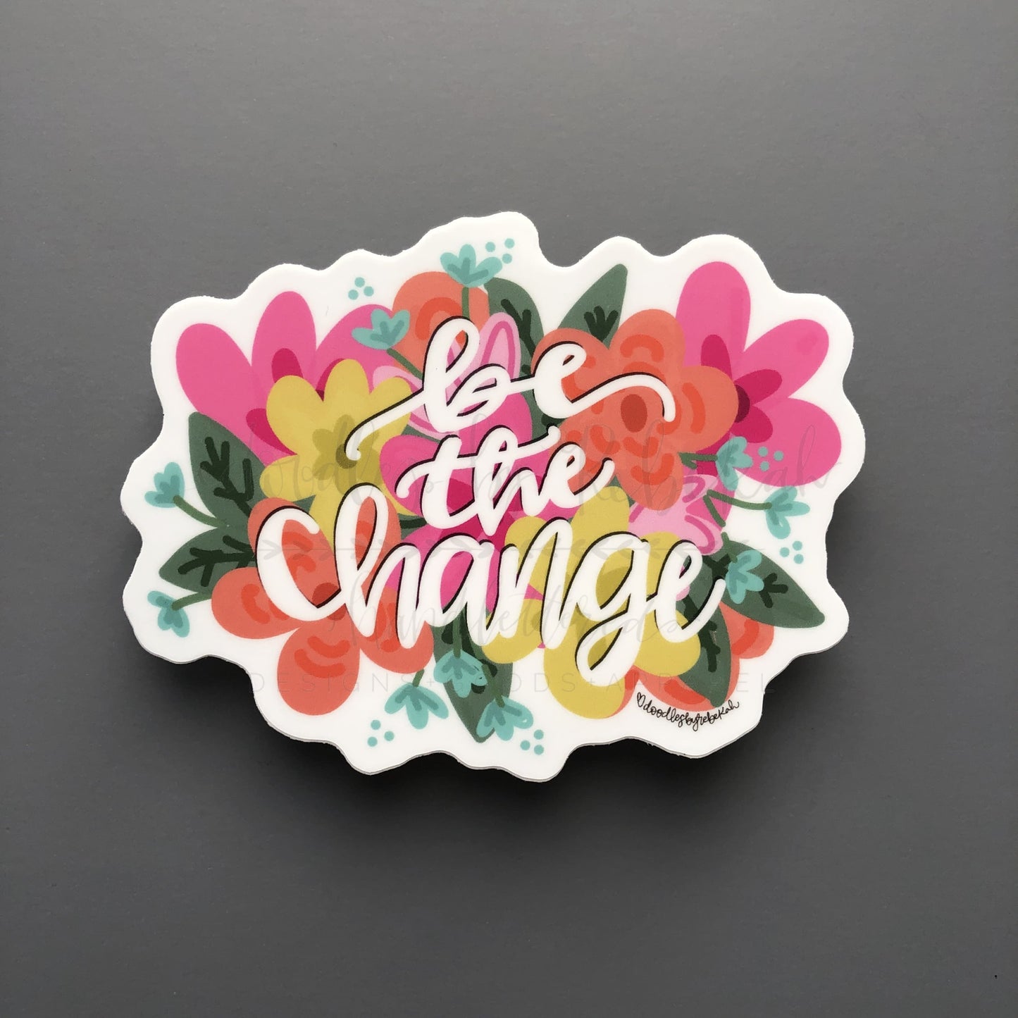A sticker with a floral border and the text 'Be The Change' in the center.