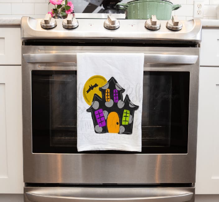 Halloween haunted house tea towel with hand-drawn spooky graphics and vibrant colors, perfect for festive kitchen decor and seasonal home styling.