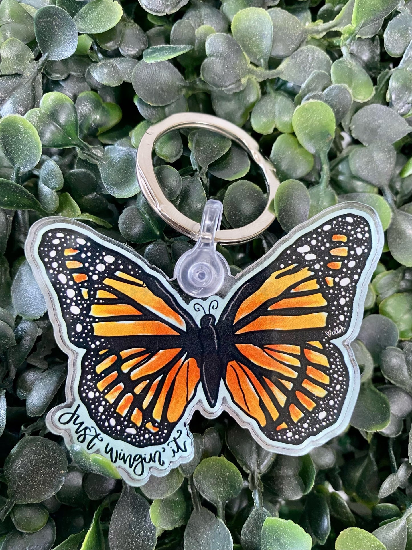 an acrylic keychain with a monarch butterfly that says "just wingin' it"