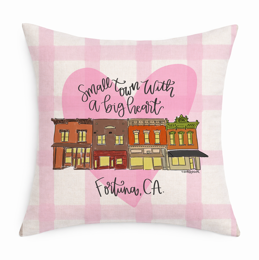 A gingham pillow with a handdrawn heart and town that says "Small Town with a big heart"