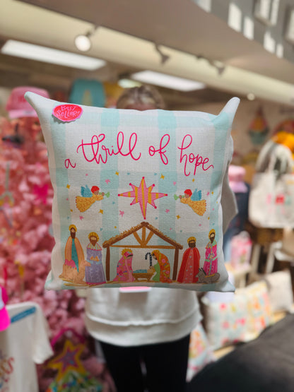 Decorative pillow with nativity scene design and 'a thrill of hope' text in a store setting.
