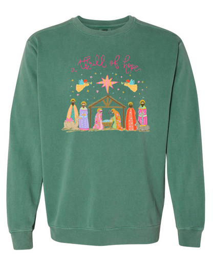 Green sweatshirt with nativity scene design and 'a thrill of hope' text on a white background