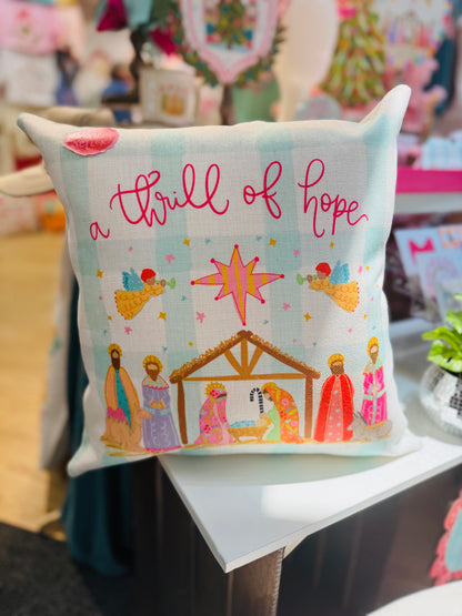 Decorative pillow with nativity scene illustration and text 'a thrill of hope' on a table.