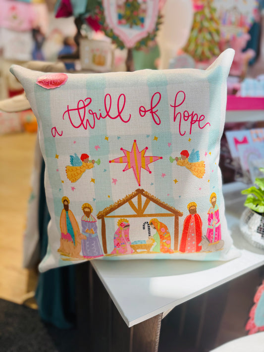 Decorative pillow with nativity scene illustration and text 'a thrill of hope' on a table.