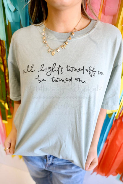 a woman showing off a light great t-shirt with the words "all lights turned off can be turned on"