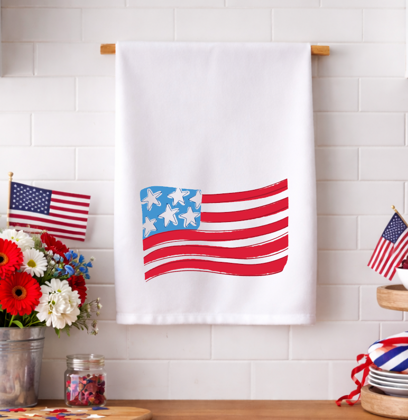 Patriotic American flag tea towel with a whimsical hand-drawn design displayed in a bright kitchen with red, white, and blue decorations.