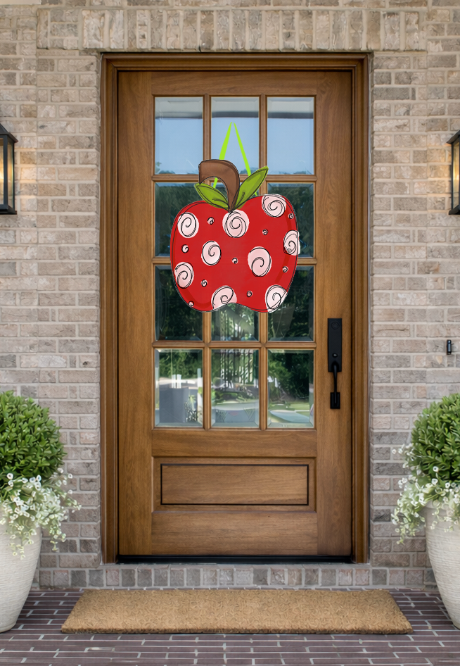Doodles by Rebekah back-to-school door decor featuring a whimsical red apple illustration with swirl patterns on a rustic front porch.
