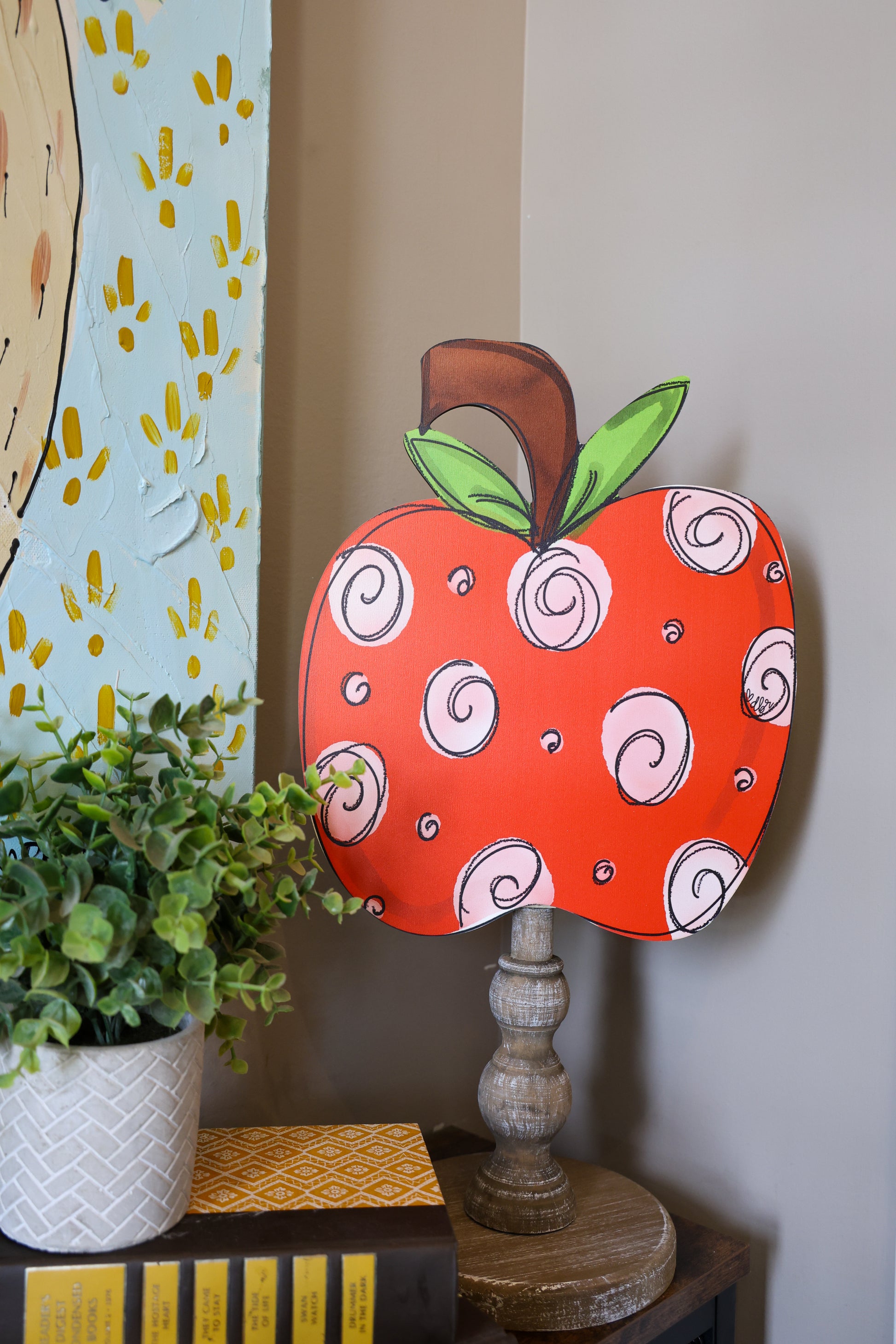 Decorative apple-shaped object with spiral patterns on a shelf next to a plant.