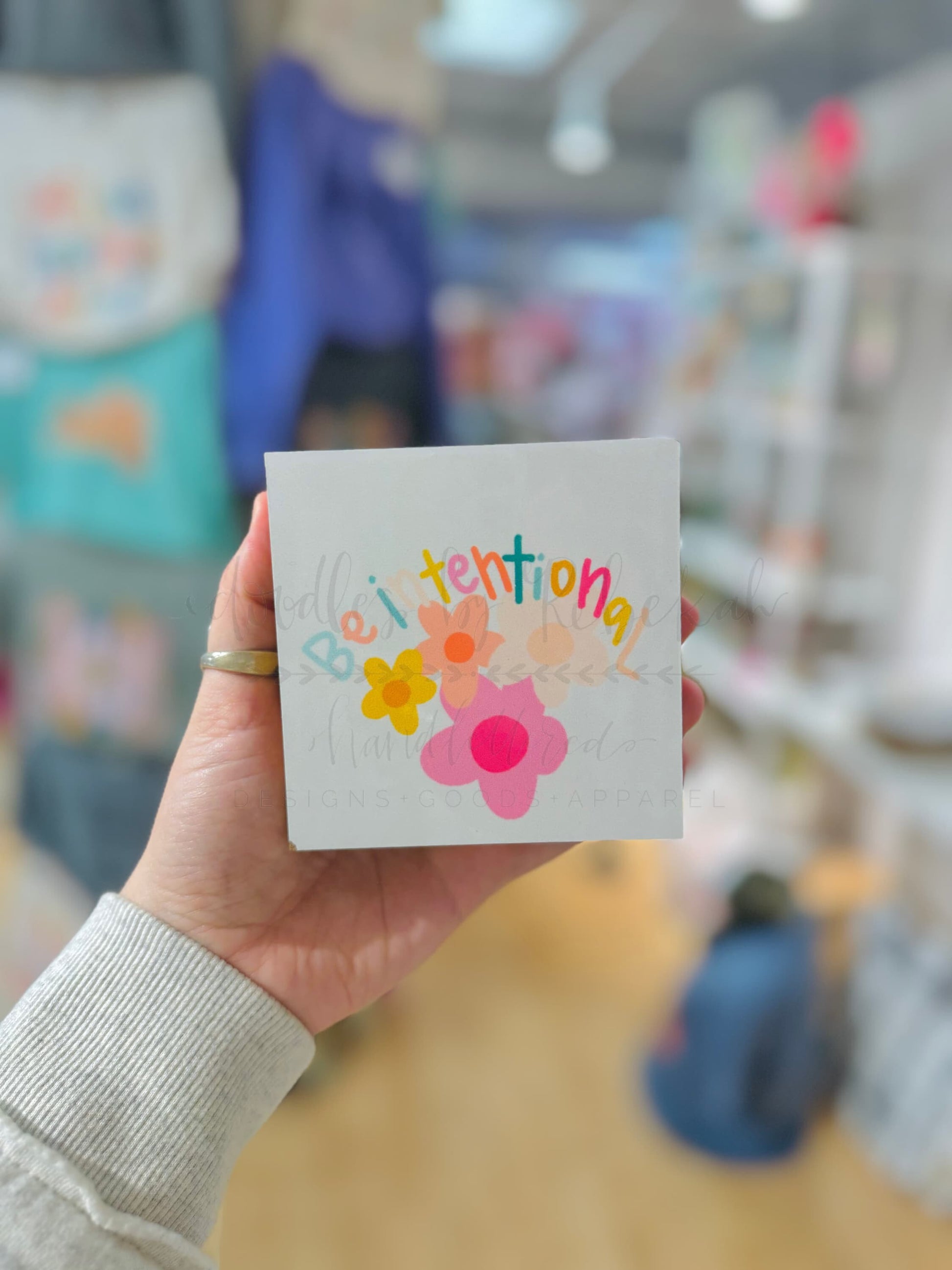 A person holding a white block with a flower graphic and the phrase "Be intentional" on it