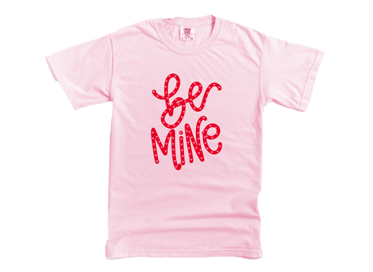 Pink t-shirt with 'Be Mine' text in red on a white background