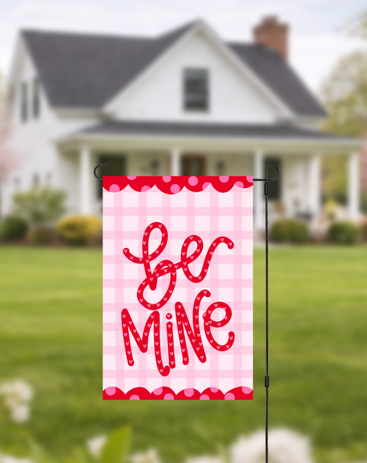 Doodles by Rebekah "Be Mine" Valentine's Day garden flag featuring whimsical hand-painted typography and a pink checkered pattern. This romantic outdoor holiday decor is perfect for Valentine's Day celebrations or adding a festive touch to front yard landscaping.