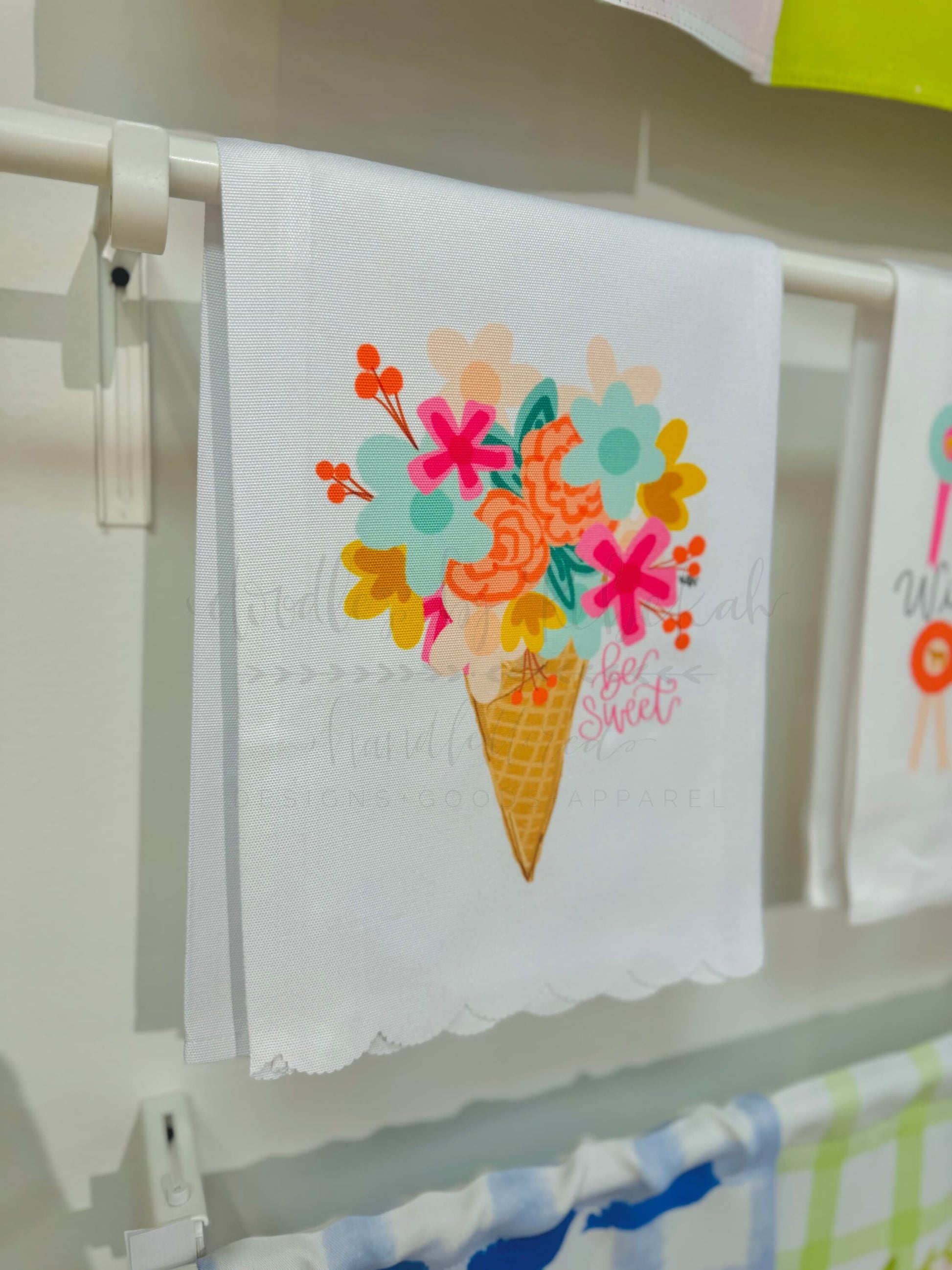 A white polyester tea towel with a colorful floral design, hanging on a rack.