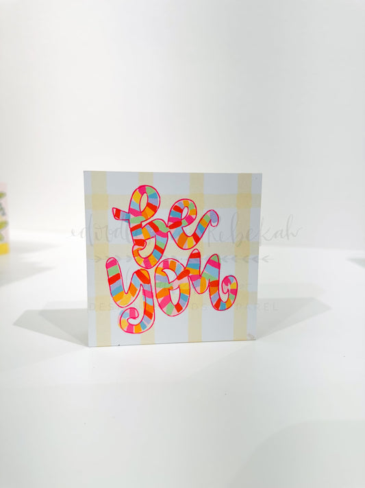 A white block with a colorful graphic with words 'be you' against a white background