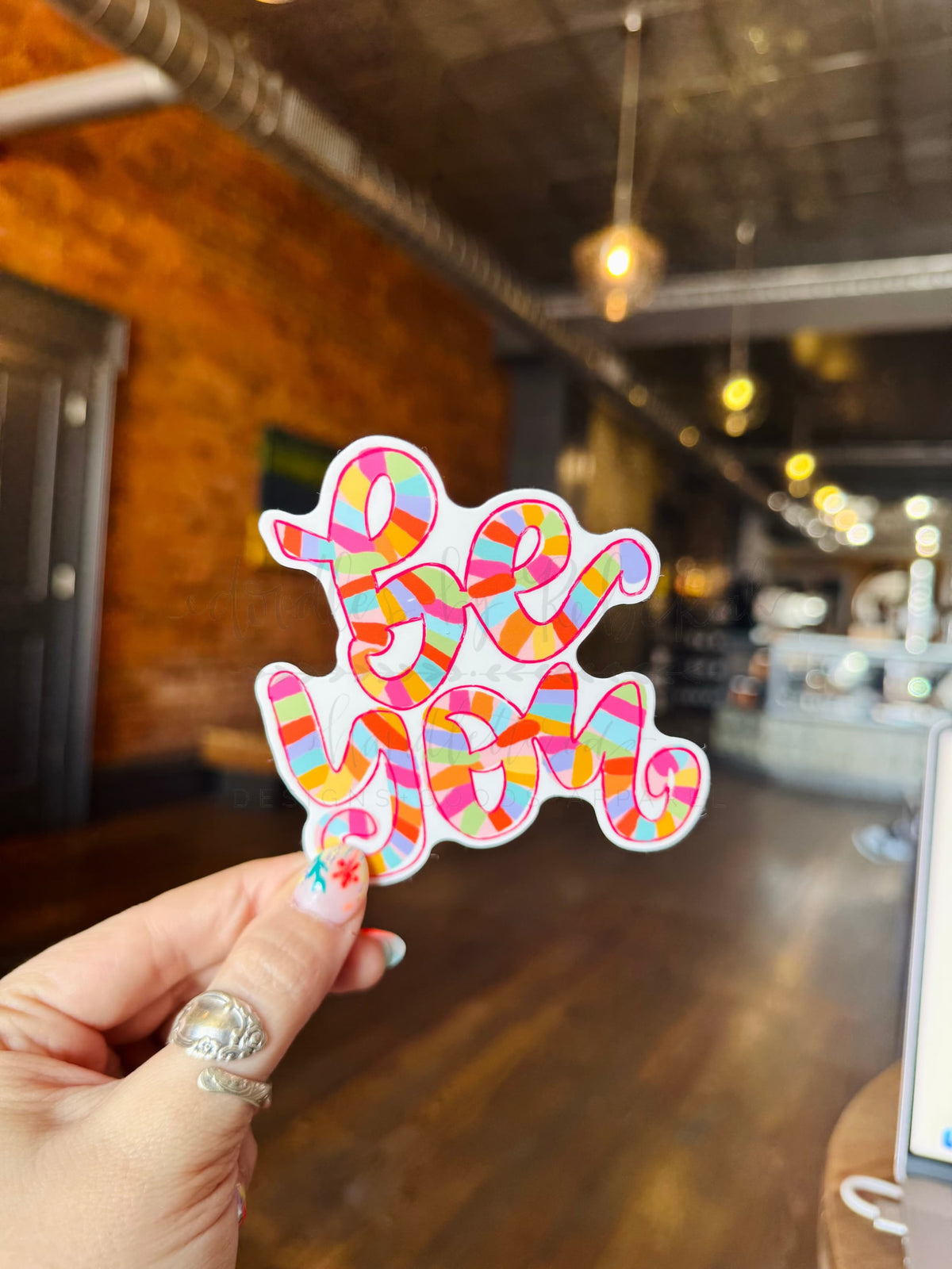 A multicolored, abstract design sticker held between fingers with a blurred background.