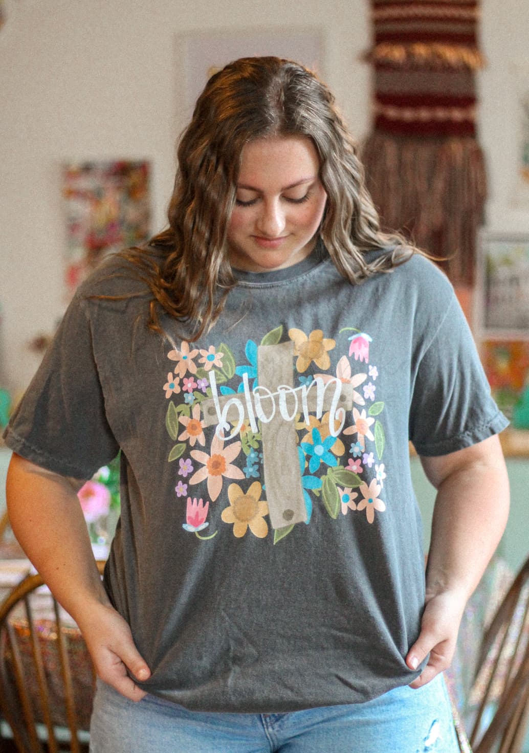 A person wearing a gray t-shirt with a floral design and the word 'bloom' in the center.