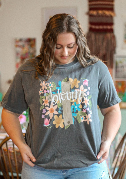 A person wearing a gray t-shirt with a floral design and the word 'bloom' in the center.