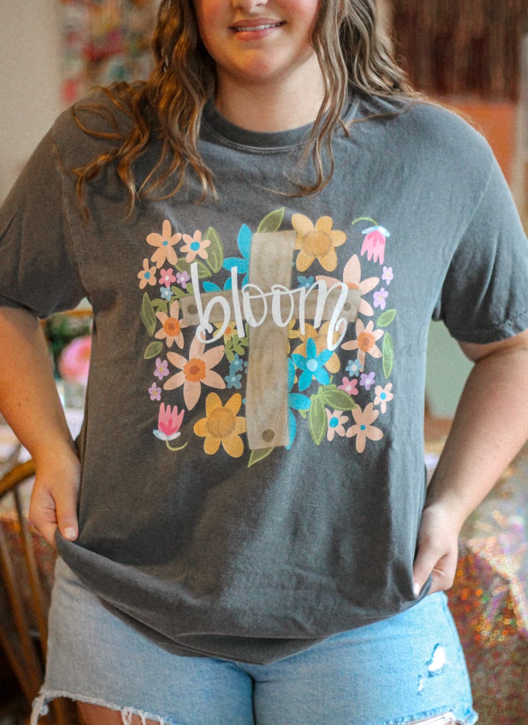 A person wearing a gray t-shirt with a floral design and the word 'bloom' in the center.