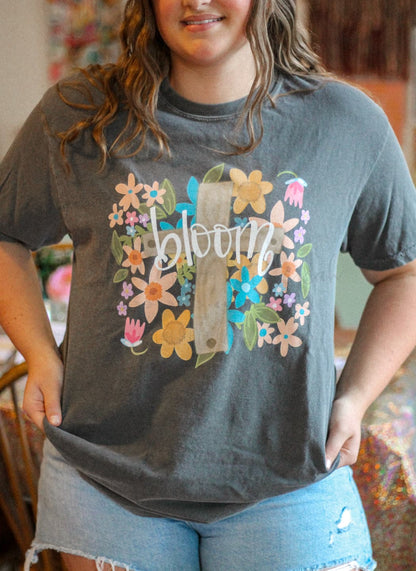 A person wearing a gray t-shirt with a floral design and the word 'bloom' in the center.