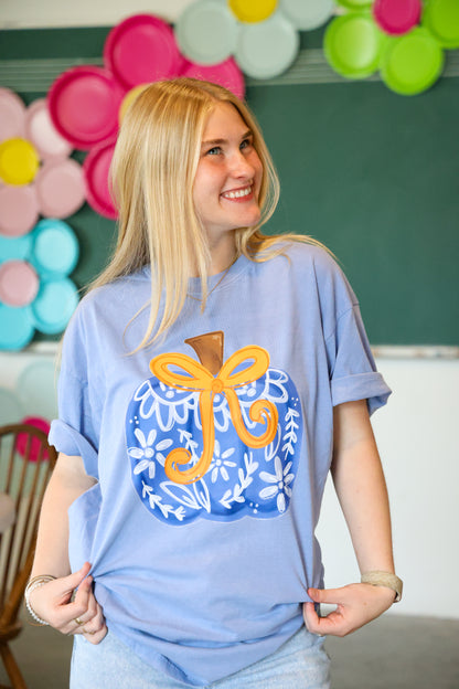 Person wearing a blue t-shirt with a decorative design, standing in front of colorful balloons and a chalkboard.