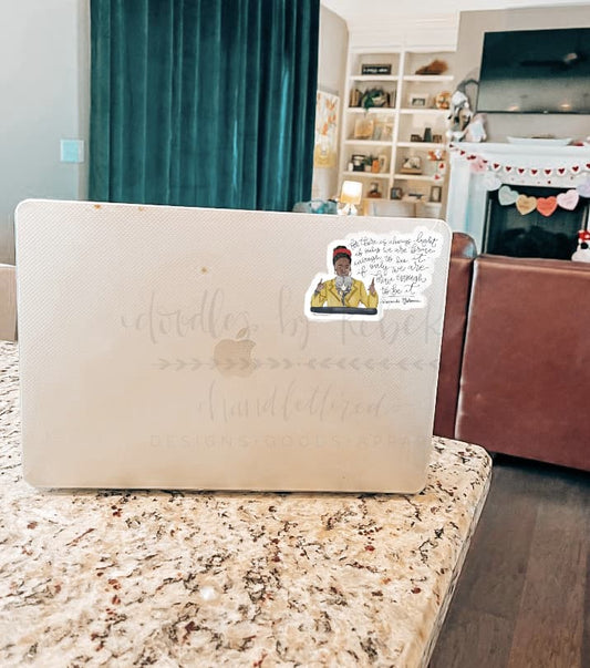 A sticker with a character illustration placed on a laptop, in a home setting.
