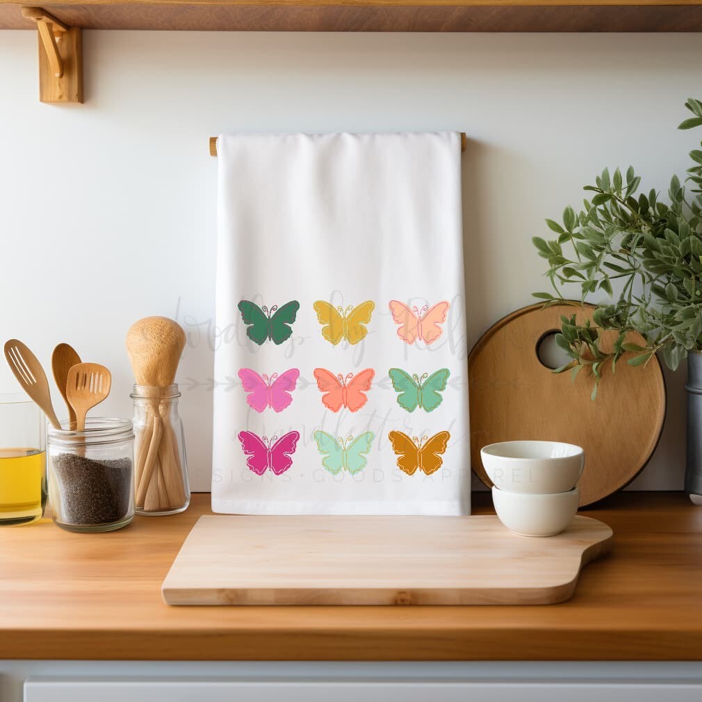 A white square tea towel with a colorful butterfly pattern, displayed on a wooden kitchen counter.