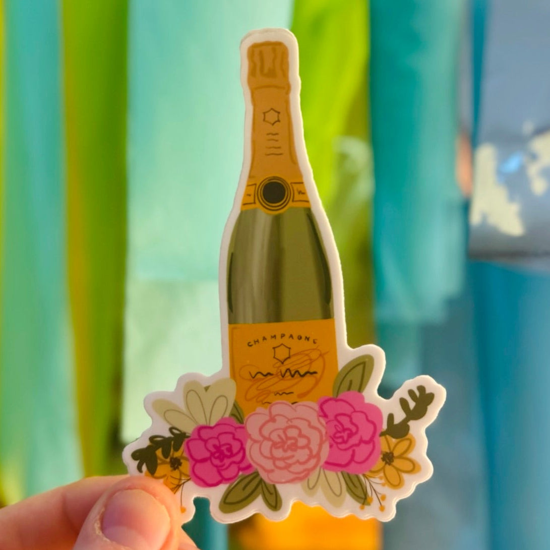Doodles by Rebekah champagne bottle and flowers vinyl sticker. This whimsical hand-painted celebration decal features a bubbly bottle with floral accents, making it a perfect gift for weddings, graduations, or New Year's Eve to decorate water bottles, laptops, and bar carts.
