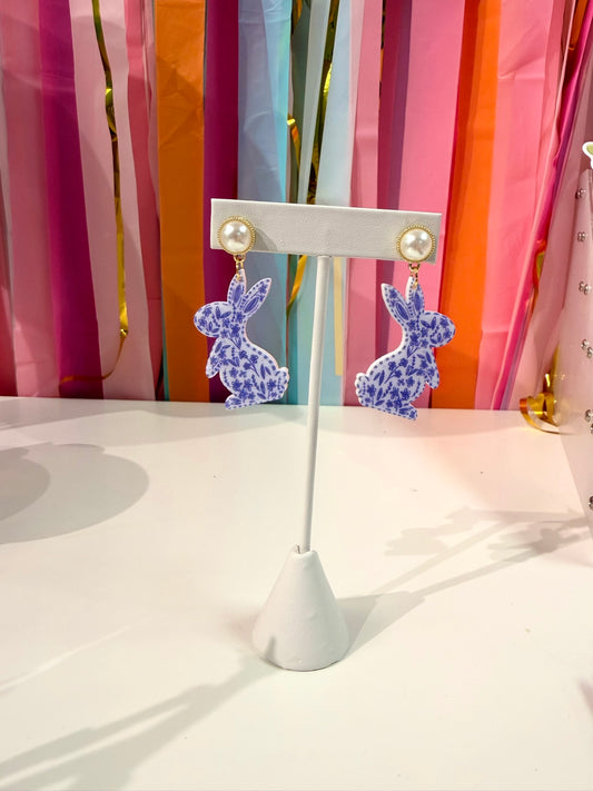 Doodles by Rebekah chinoiserie bunny earrings featuring hand-drawn navy and white floral patterns and pearl studs. These whimsical ginger jar-inspired spring accessories are shown against a bright party streamer backdrop.