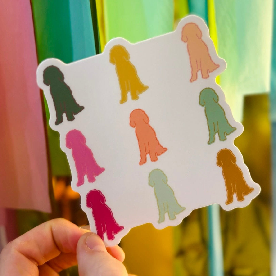 Doodles by Rebekah colorful dog silhouette sticker. This whimsical hand-painted vinyl decal features multiple dog breed silhouettes in various bright colors, making it an ideal gift for dog lovers to use for personalizing water bottles, laptops, and planners.