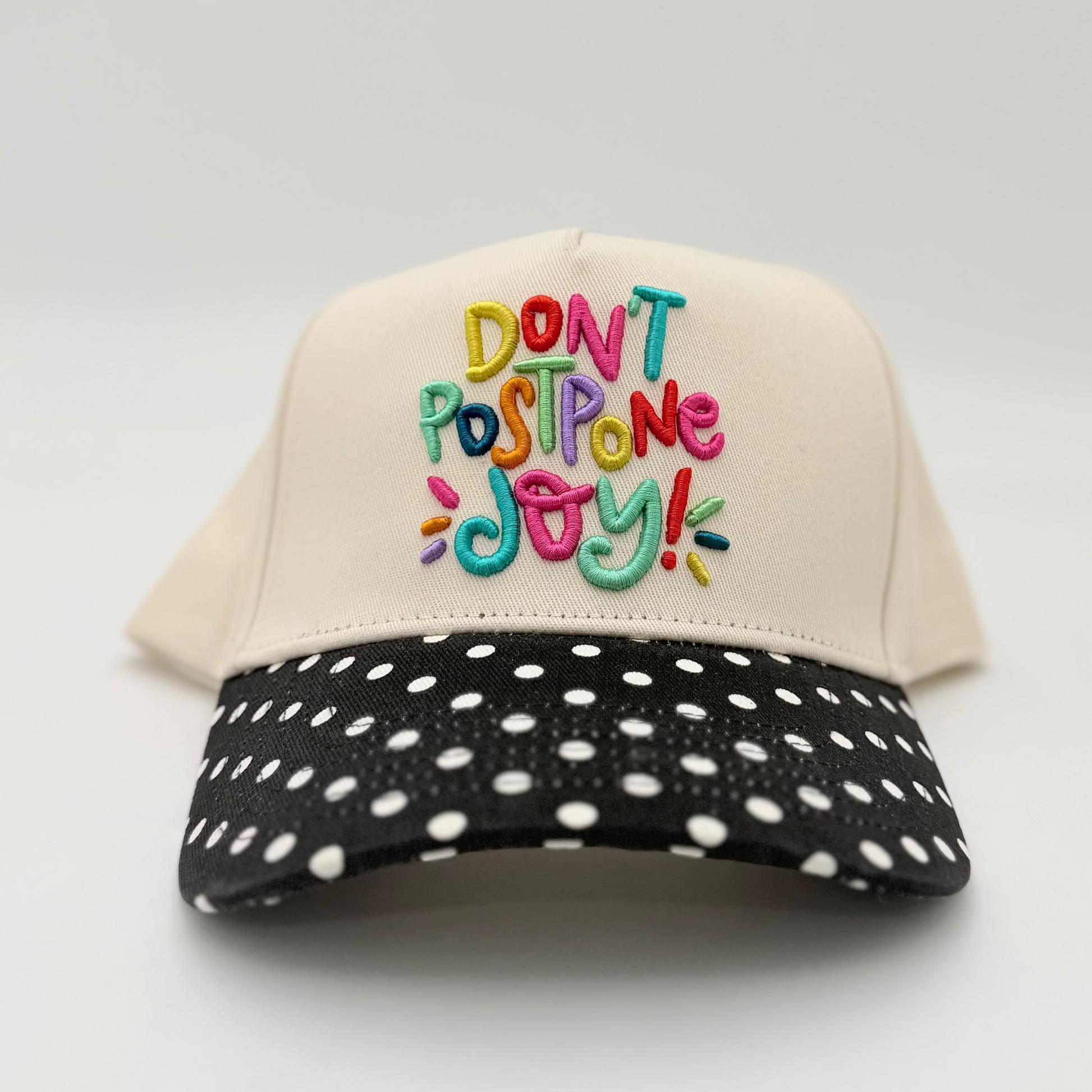 Cap with colorful text 'DON'T POSPONE JOY!' on a white background