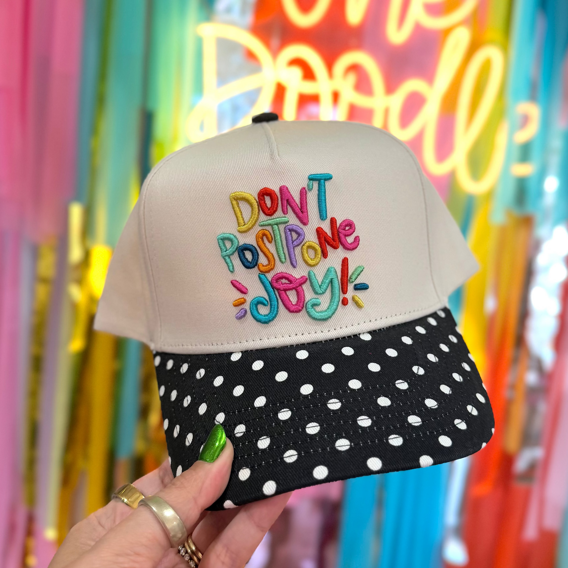 Cap with colorful text held in front of a festive background with balloons and 'One Doodle' sign.