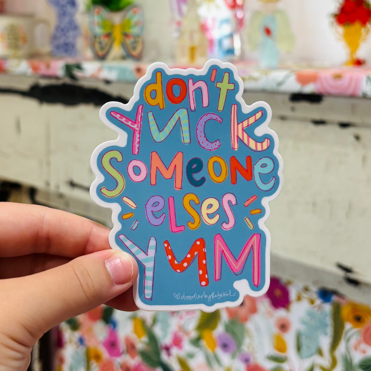 a hand holding sticker that reads "Don't Yuck Someone Else's Yum"