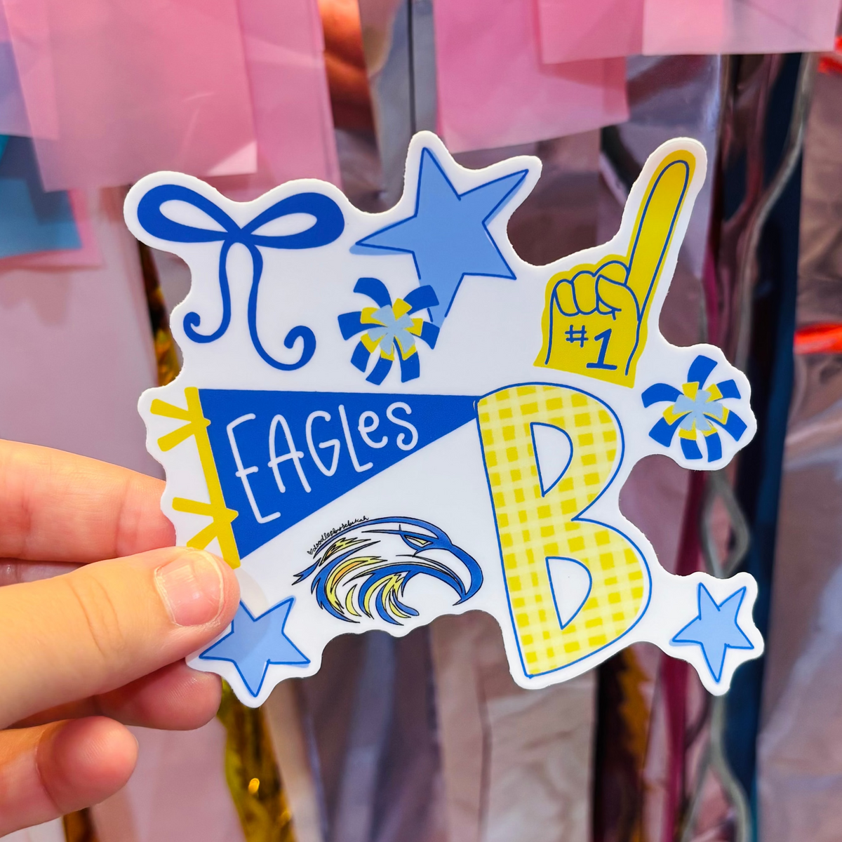 a hand holding a blue and yellow sticker with Team Eagles hand draw iconography 