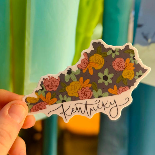 Doodles by Rebekah floral Kentucky state silhouette sticker. This whimsical botanical vinyl decal features a hand-painted wildflower pattern and elegant script, making it a beautiful state pride gift for decorating water bottles, laptops, and planners.